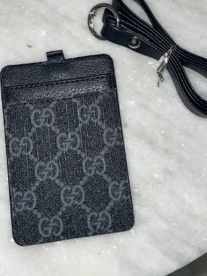 Svart plånbok - Säljer en stilren svart plånbok från P med klassisk trekantig metallogo framtill. Väskan är tillverkad i slitstarkt syntetmaterial och kommer med en matchande svart axelrem med metallspänne. Perfekt för att bära det viktigaste på ett snyggt sätt.