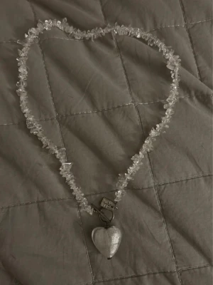 Halsband med genomskinliga pärlor och hjärthänge - Unikt halsband med genomskinliga pärlor och ett stort silverfärgat hjärthänge. Kedjan har även en liten bricka med texten 'dag/natt'.