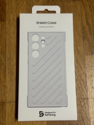Grått Shield Case till Galaxy S24 Ultra - Snyggt och tåligt mobilskal i grått för Samsung Galaxy S24 Ultra. Skalet har diagonala ränder för extra grepp och stilren look. Designat för att skydda mobilen mot stötar och repor. Perfekt passform med utskärningar för kameror och knappar.