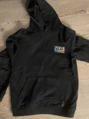 Svart hoodie från Vans med tryck - Svart hoodie från Vans. Stor färgglad 'Off The Wall Vans'-grafik på ryggen. Mjuk bomullsmix, huva och stor magficka framtill. Hoodien är i storlek L i barnstorlek så den är som en XS 💕
