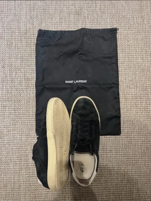 Svarta Saint Laurent sneakers i mocka - Svarta sneakers från Saint Laurent i mjuk mocka med svarta skosnören och vit sula. Klassisk låg modell med stilren design och diskreta detaljer. Kommer med original dustbag. Perfekta för dig som gillar lyxiga och minimalistiska sneakers.
