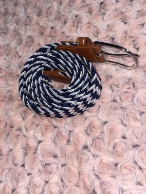  flätat bälte /randigt  - Snyggt flätat bälte i marinblått och vitt med bruna läderdetaljer och silverfärgat spänne. Perfekt accessoar för att lyfta din outfit med en cool och modern touch. Passar till jeans, kjol eller shorts.