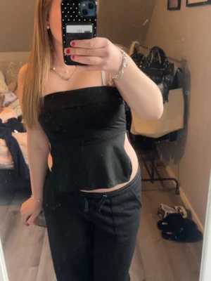 Svart axelbandslös tubtopp - Snygg svart axelbandslös tubtopp med figurnära passform och lätt utsvängd nederkant. Toppen är ärmlös och har en enkel, stilren design som passar perfekt till många olika outfits.