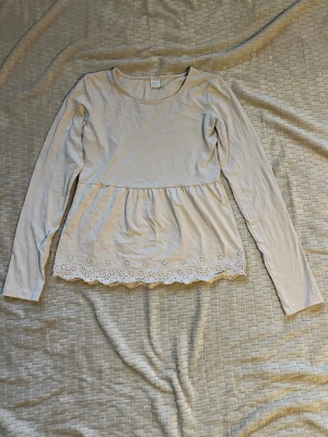 Gammelrosa långärmad topp med spetskant - Söt gammelrosa långärmad topp med rund hals och volang nedtill. Nederkanten har en fin spetsdetalj med broderade blommor och vågig kant. Den ser ljusare ut på bilderna än i verkligheten. Endast andvänd ett fåtal gånger. Mått: Längd 60cm, Bredd under armarna 44cm, Bredd nertill 49cm. Material: Bomull och elastan.