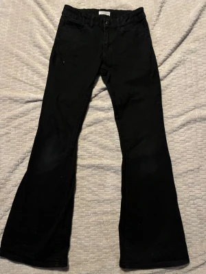 Svarta bootcut jeans från Lindex - Säljer ett par svarta bootcut jeans från Lindex. Jeansen har klassisk femficksmodell, normal midja och utsvängda ben. Materialet är mjukt och stretchigt för extra komfort. Sömmen vid knapphålet har gått upp men det syns inte när knappen är stängd. Midjan är ställbar. 
