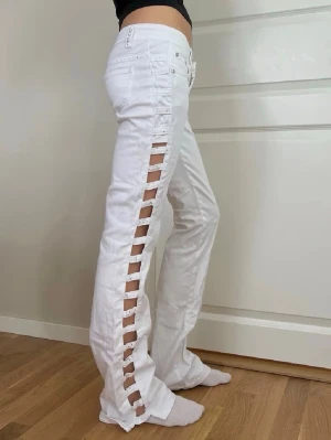 Vita jeans med cut-out detaljer - Säljer ett par vita jeans med unika cut-out detaljer längs hela sidorna. Jeansen har klassisk femficksmodell och normal midja. Materialet är denim i bomull och de har knapp- och dragkedjestängning framtill. Perfekta för dig som vill sticka ut!