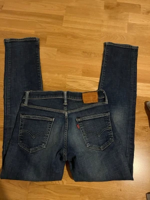 Levi's 511 mörkblå jeans - Säljer ett par klassiska Levi's 511 jeans i mörkblå tvätt med raka ben och femficksmodell. Jeansen har snygga slitningar och den ikoniska läderlappen bak i midjan. Perfekta för dig som gillar en tidlös och avslappnad stil. Passar nog bra för mindre än S om man har det.