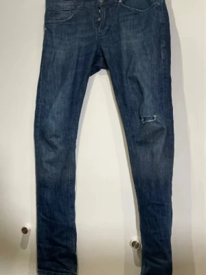 Dondup  - Snygga mörkblå skinny jeans med slitning på höger knä och bakficka. Klassisk femficksmodell med knappgylf och smal passform. Perfekta för en avslappnad streetstil. Tillverkade i denim med lätt stretch för skön känsla.