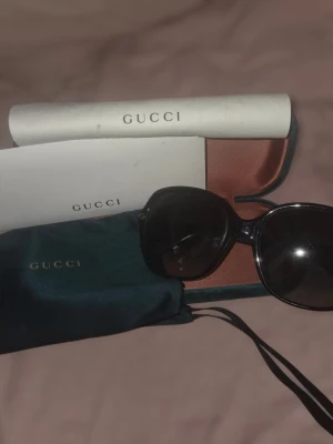 Svarta solglasögon från Gucci - Stilrena svarta solglasögon från Gucci med klassisk rundad form. Kommer med originalfodral, putsduk och certifikat. Snygg och tidlös accessoar som lyfter vilken outfit som helst. Putsduken är väl använd 