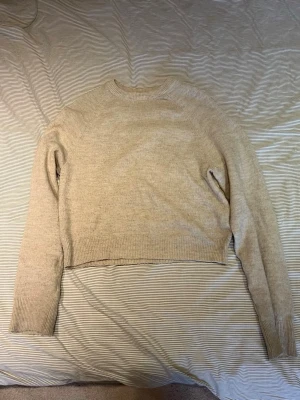 Beige stickad tröja - En ljus-beige stickad tröja med croppad passform och rund hals. Tröjan har långa ärmar och ribbade muddar vid ärmslut och nederkant. 