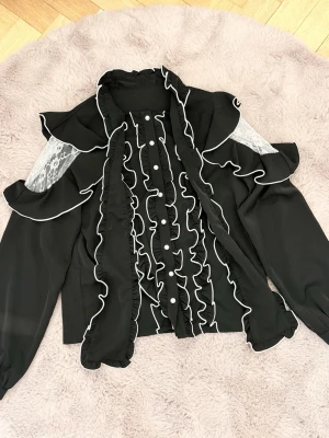 Svart volangblus  Ma*rs jirai kei - svart blus med långa ärmar, volangdetaljer och vita sömmar. I mycket gott skick, från ma*rs