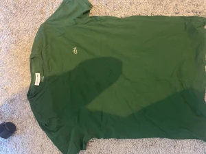 Grön t-shirt från Lacoste - Snygg grön t-shirt från Lacoste i 100% pima bomull. Klassisk passform med korta ärmar och den ikoniska krokodilloggan broderad på bröstet. Perfekt till jeans eller shorts för en clean och stilren look.