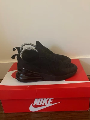 Nike Air Max 270 helsvarta sneakers - Nike Air Max 270 sneakers i helsvart med mesh-ovandel och stor synlig Air-enhet i hälen. Snygg sportig siluett med klassisk Nike-logga och sköna snören. Perfekta för dig som gillar streetwear och vill ha en clean look.