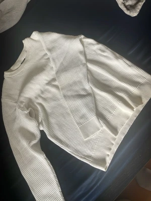Vit stickad tröja med struktur - Säljer en vit stickad tröja med snygg struktur och rund hals. Tröjan har långa ärmar och ribbade muddar vid ärmslut och nederkant. Perfekt för dig som gillar en clean och stilren look. Helt ny