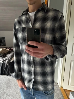 Svartvit rutig skjorta - Säljer en svartvit rutig skjorta med klassisk krage och bröstficka. Skjortan har lång ärm och knäppning framtill. Perfekt för en avslappnad och stilren look. Passar till jeans eller chinos.