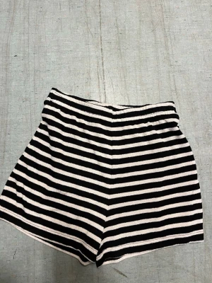 Randiga shorts i svart och vitt - Säljer ett par randiga shorts med svart och vitt mönster. De har en hög midja och är tillverkade i ett mjukt, stretchigt material som känns bekvämt. Perfekta för varma dagar och enkel att matcha med olika toppar.