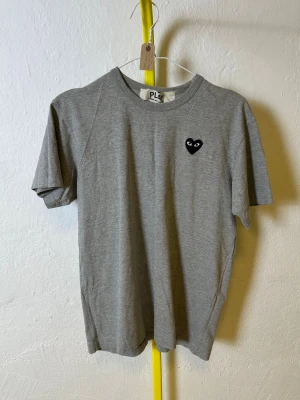Grå t-shirt från Comme Des Garçons  - Denna vara kommer att auktioneras ut på Plick Live den 3 juni klockan 19:00
