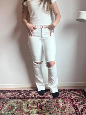 Vita bootcut H&M jeans - Säljer dessa medelhögmidjade, bootcut jeans med klippta hål på från H&M. Storlek 36 och i ett mycket fint skick. 