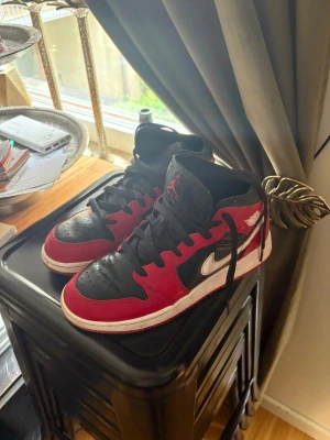 Air Jordan 1 Mid röd/svart/vit - Säljer ett par Air Jordan 1 Mid sneakers i klassisk röd, svart och vit färg. Skorna har svart tåparti och snörning, röd ovandel och vita detaljer som Swoosh och Air Jordan-logga på sidan. Tillverkade i läder och textil för en ikonisk streetwear-look. Använda ett par gånger fast skorna är inte sönder nånstans och har ingen skador 