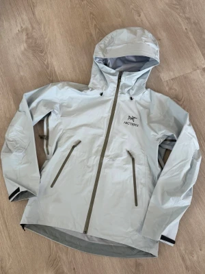 Baby blue Arc'teryx rain jacket - Stylish light grey rain jacket from Arc'teryx with hood and waterproof zippers. The jacket has two slanted pockets at the front, adjustable cuffs and a minimalist design. gore-tex material Mens size M but fits S