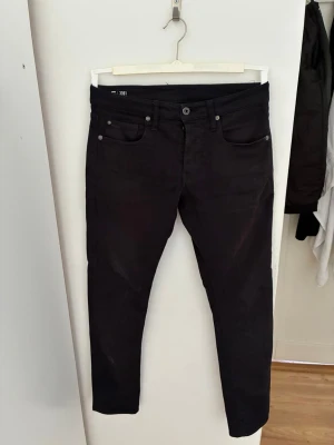 (Storlek midja29)(längd 32)Svarta slimfit jeans från G-Star RAW - Säljer ett par svarta slim fit jeans från G-Star RAW med klassisk femficksdesign och snygga detaljer. Jeansen har en smal passform och är tillverkade i stretchigt material för extra komfort. Perfekta för en trendig och avslappnad stil.