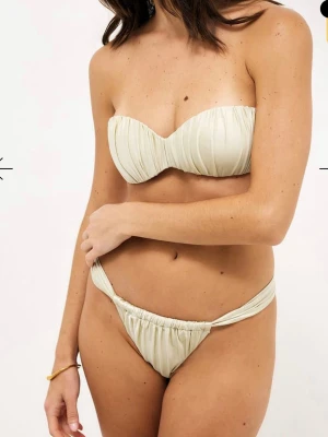 Beige bandeau bikini med rynkade detaljer - Trendig beige bandeau bikini med rynkade detaljer och avtagbara axelband. Överdelen är axelbandslös men kan bäras med smala band, och bikinitrosan har en twistad kant. Perfekt för strandhäng och soliga dagar. Helt nya med prislapp kvar💞