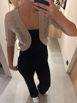 Beige kort bolero med hålmönster - Säljer en guldig, glittrig kort bolero med hålmönster och halvlånga ärmar. Tröjan har en öppen front och bred ribbad kant🌸
