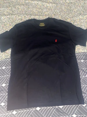 Svart t-shirt från Polo Ralph Lauren - Snygg svart t-shirt från Polo Ralph Lauren med klassisk röd logga broderad på bröstet. Modellen är slim fit och tillverkad i 100% bomull för en skön känsla. Perfekt basplagg med enkel design och rund hals.