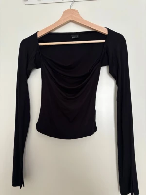 Svart långärmad topp från Gina Tricot - Säljer en svart långärmad topp från Gina Tricot  som har figurnära passform. Toppen har en bred, något fyrkantig urringning och är tillverkad i ett stretchigt syntetmaterial som sitter snyggt på kroppen.