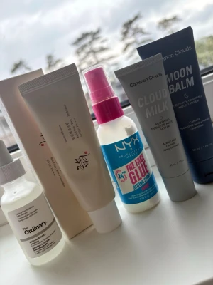 Hudvårdsprodukter från The Ordinary, NYX & Common Clouds - Säljer ett kit med hudvårdsprodukter: serum från The Ordinary, setting spray från NYX med rosa lock samt Cloud Milk och Moon Balm från Common Clouds. Produkterna har olika former på flaskor och tuber, i vitt, blått och rosa. Perfekt för dig som vill boosta din hudvårdsrutin.