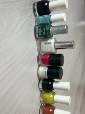Nagellack mix i flera färger - Säljer ett set med nagellack i olika färger och märken. Färgerna inkluderar svart, turkos, grön med glitter, vitt, rosa, beige, mörkblå, gul och terrakotta. Flera olika flaskformer och lock, både matta och glansiga lack. Perfekt för dig som vill variera din nagelstil.
