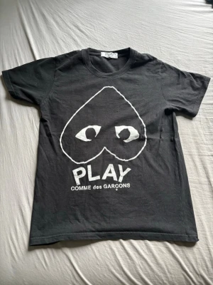 Svart Comme des Garçons PLAY t-shirt - Cool svart t-shirt från Comme des Garçons PLAY med det ikoniska hjärtmotivet och ögon framtill. T-shirten har rund hals, korta ärmar och är gjord i mjuk bomull. Perfekt för dig som gillar streetwear och vill sticka ut med en unik design.