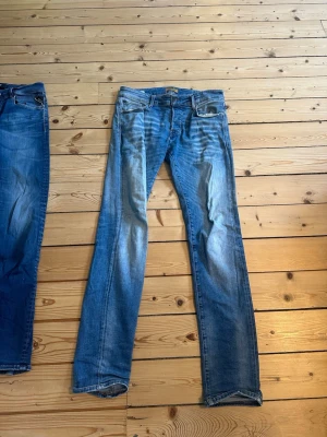 Blå raka jeans med slitningar - Säljer ett par klassiska blå Jack and Jones jeans med raka ben och snygga slitningar framtill. Jeansen har fem fickor, normal midja och är tillverkade i denim. Perfekta för en avslappnad och trendig look.