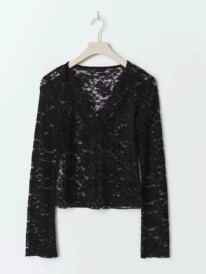 Svart spetsblus med v-ringning - Snygg svart blus i genombruten spets med v-ringad hals och långa ärmar. Perfekt för dig som gillar en trendig och elegant look. Blusen är lätt croppad och har en feminin siluett.