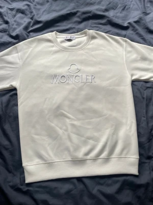 Vit sweatshirt från Moncler - Snygg vit sweatshirt från Moncler med broderad logga på bröstet och klassiskt Moncler-märke på ärmen. Tröjan har rund halsringning, ribbade muddar och är tillverkad i mjukt bomullsmaterial. Perfekt för en clean och stilren look.