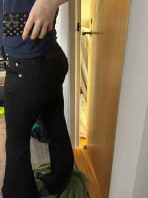 Svarta bootcut jeans - Säljer ett par svarta bootcut jeans med klassisk femficksdesign och silverfärgade knappar. Jeansen har en snygg utsvängd passform nedtill och är tillverkade i ett stretchigt denimtyg som sitter bekvämt. Perfekta för dig som gillar en tidlös och trendig look.