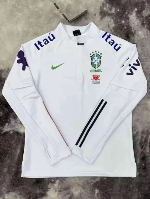 Vit Brasilien träningströja Nike - Vit långärmad träningströja från Nike med Brasilien CBF-logga på bröstet. Tröjan har blå och gröna detaljer, halv dragkedja framtill och tryckta sponsorloggor på ärmar och axlar. Perfekt för fotbollsträning eller sportig stil.