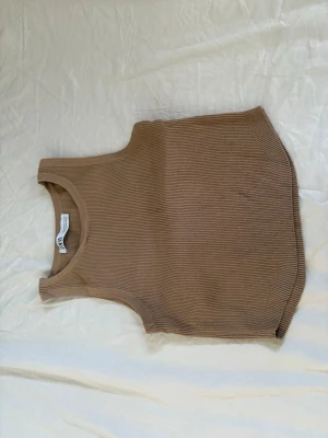 Beige ribbad linnetopp från Zara - Säljer en beige ribbad linnetopp från Zara. Toppen är ärmlös och har en rund halsringning. Materialet är mjukt och stretchigt, perfekt för lager på lager eller till jeans. Enkel och stilren design som passar till det mesta.