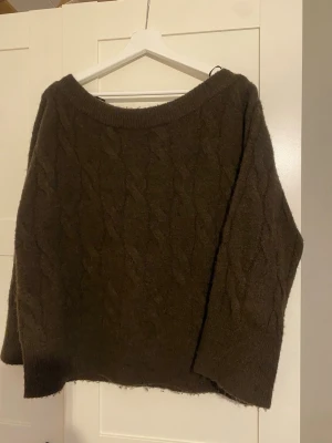 Mörkbrun kabelstickad tröja - Mysig mörkbrun stickad tröja med kabelstickat mönster och bred halsringning. Vill varna för att den sticks lite gran ( är dock väldigt känslig för ull) men funkar bra om man har ett linne under. Från Gina i storlek 158/164 