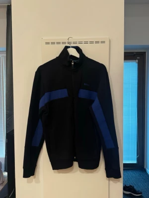 Svart och blå hoodie från Hugo BOSS - *HERR*  Svart tröja med blå ränder från Hugo Boss.   Storlek S.   Bra skick inget att anmärka