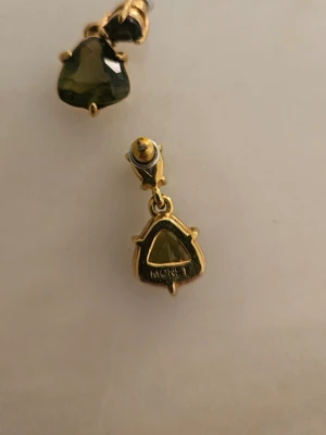 Guldtonade örhängen med gröna stenar - Snygga örhängen från Monet i guldtonad metall med triangulära gröna stenar. De har en unik form och elegant infattning som ger en cool och trendig vibe. Perfekta för att lyfta din stil med lite extra färg och glans.