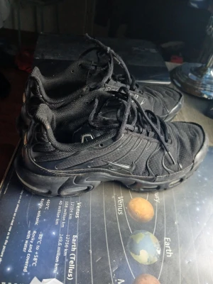 Nike Air Max Plus svarta sneakers - Säljer ett par helsvarta Nike Air Max Plus sneakers med klassisk TN-logga på hälen. Skorna har mesh- och syntetmaterial, synlig Air-dämpning i sulan och vågiga detaljer längs sidorna. Perfekta för dig som gillar streetwear och sportig stil. Det är ett hål  i skor men den går använd och det finns inga sulor. Skorna är har slitage men det går använda dom.