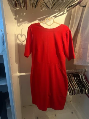 Röd kort klänning med dragkedja - Snygg röd klänning med kort ärm och rund halsringning. Klänningen har en figurnära passform och dragkedja i ryggen. Perfekt för dig som vill sticka ut med en enkel men stilren look.