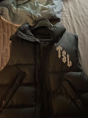 Svart dunväst från Trapstar XS - Säljer en svart dunväst från Trapstar i nytt skick utan några skador.. Västen har hög krage, dragkedja framtill och är vadderad för extra värme. Perfekt för lager på lager och streetwear-stil.
