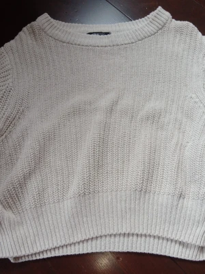 Beige/vit cropped stickad tröja - Säljer en beige/vit cropped stickad tröja med rund halsringning och breda ribbade muddar. Tröjan har en avslappnad passform och är perfekt för lager på lager. Materialet känns mjukt och bekvämt.
