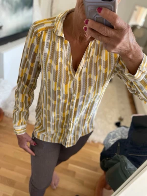 Mönstrad skjorta i gult och vitt - Snygg skjorta med grafiskt mönster i gult, vitt och grått. Skjortan har klassisk krage, knappar framtill och långa ärmar. Perfekt för dig som gillar färg och unika prints.