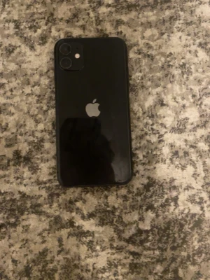 Svart iPhone 11 - Säljer en svart iPhone 11 från Apple. Telefonen har en stilren design med rundade hörn, glasbaksida och dubbla kameror på baksidan. Skärmen är stor och har en tydlig notch upptill. Perfekt för dig som vill ha en modern och snygg smartphone. Telefonen har inga skador förutom en liten repa som inte syns när man tittar på telefonen. Skall och skärmskydd ingår i köpet. Den har batteri hälsan 73%. Jätte bra mobil passa på.😊