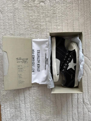 Svarta Golden Goose sneakers med stjärna (43) - Snygga svarta sneakers från Golden Goose med vit stjärndetalj på sidan och vit sula. Skorna har klassisk låg modell, svarta skosnören och tydliga kontrastsömmar. Ovandelen är i canvas och sulan i gummi. Perfekta för dig som gillar streetstyle och unika detaljer.