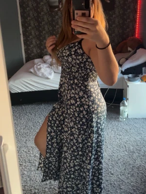 Blommig långklänning med slits - Supersnygg långklänning med mörkblå botten och små vita blommor, smala axelband och en hög slits på ena sidan. Perfekt för sommarens alla tillfällen och ger en riktigt fräsch vibe. Klänningen är från Zara och har använt klänningen en gång så den är i fint skick. Den är tajtare runt bröstet därför blir de lite svårt att dra på klänningen. Köpte först i storlek M men behövde köpa L istället för kunde inte dra över den runt brösten.( storlek b i BH ) 