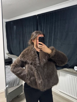 Brun fluffig pälsjacka - Säljer en brun pälsjacka med bred krage och långärmad design. Jackan är fluffig och har en klassisk, rak passform som ger en cool och trendig look. Perfekt för dig som vill ha något varmt och snyggt till hösten och vintern.